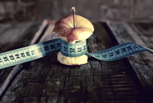 A partially eaten apple core with a blue measuring tape wrapped around its middle rests on a rustic wooden surface, symbolizing the careful measurement and healing process often found in trauma treatment. The background is blurred, emphasizing the apple as the focal point of the image.