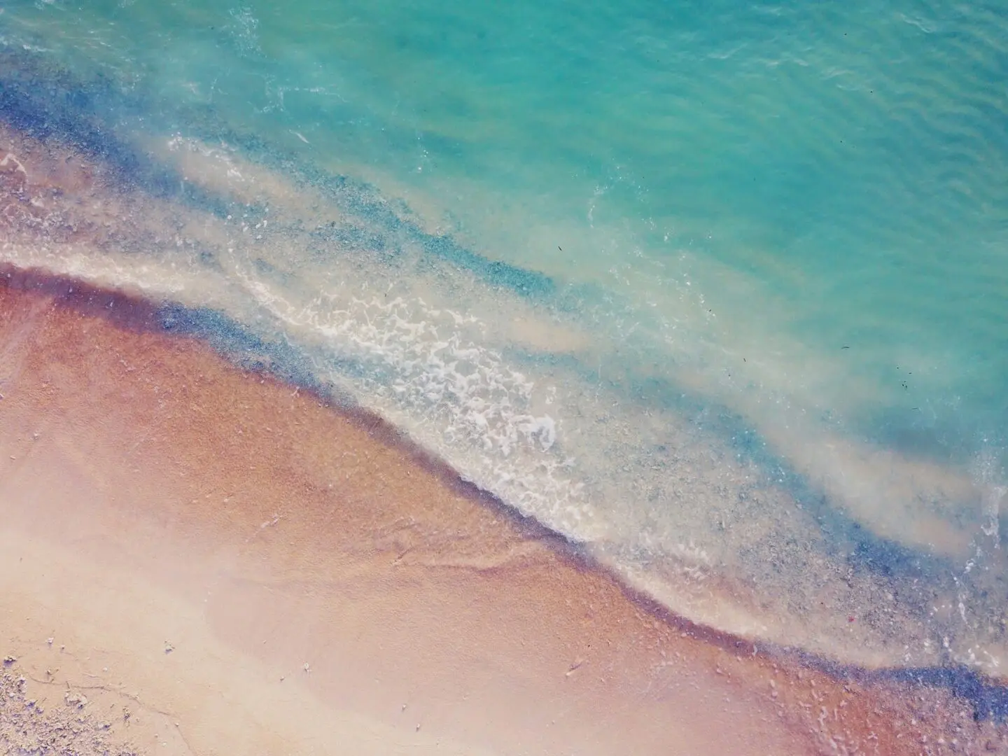 Aerial view of a serene beach with turquoise waters gently lapping against the soft, sandy shore. The water displays various shades of blue and green, creating a tranquil and picturesque seascape that emphasizes the importance of feeling safe and calm, similar to the goals in trauma therapy.