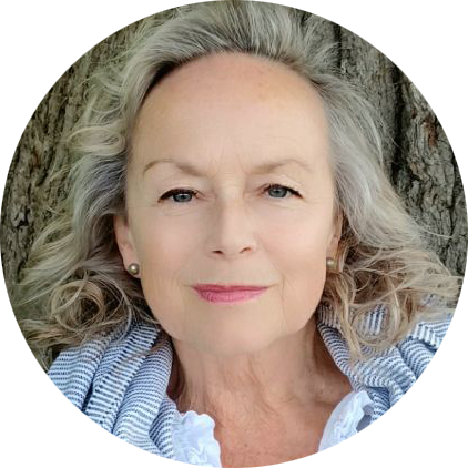 Portrait of an older woman with long, wavy gray hair, smiling softly. She is wearing a striped scarf over a white top, standing against a tree background, embodying the serene and nurturing essence often associated with Khiron Clinics' compassionate care.