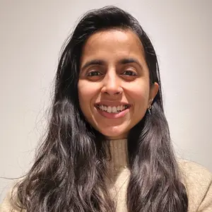 A person with long dark hair and a beige sweater smiles at the camera against a plain background, embodying the warmth and approachability that is central to Khiron Clinics' philosophy.
