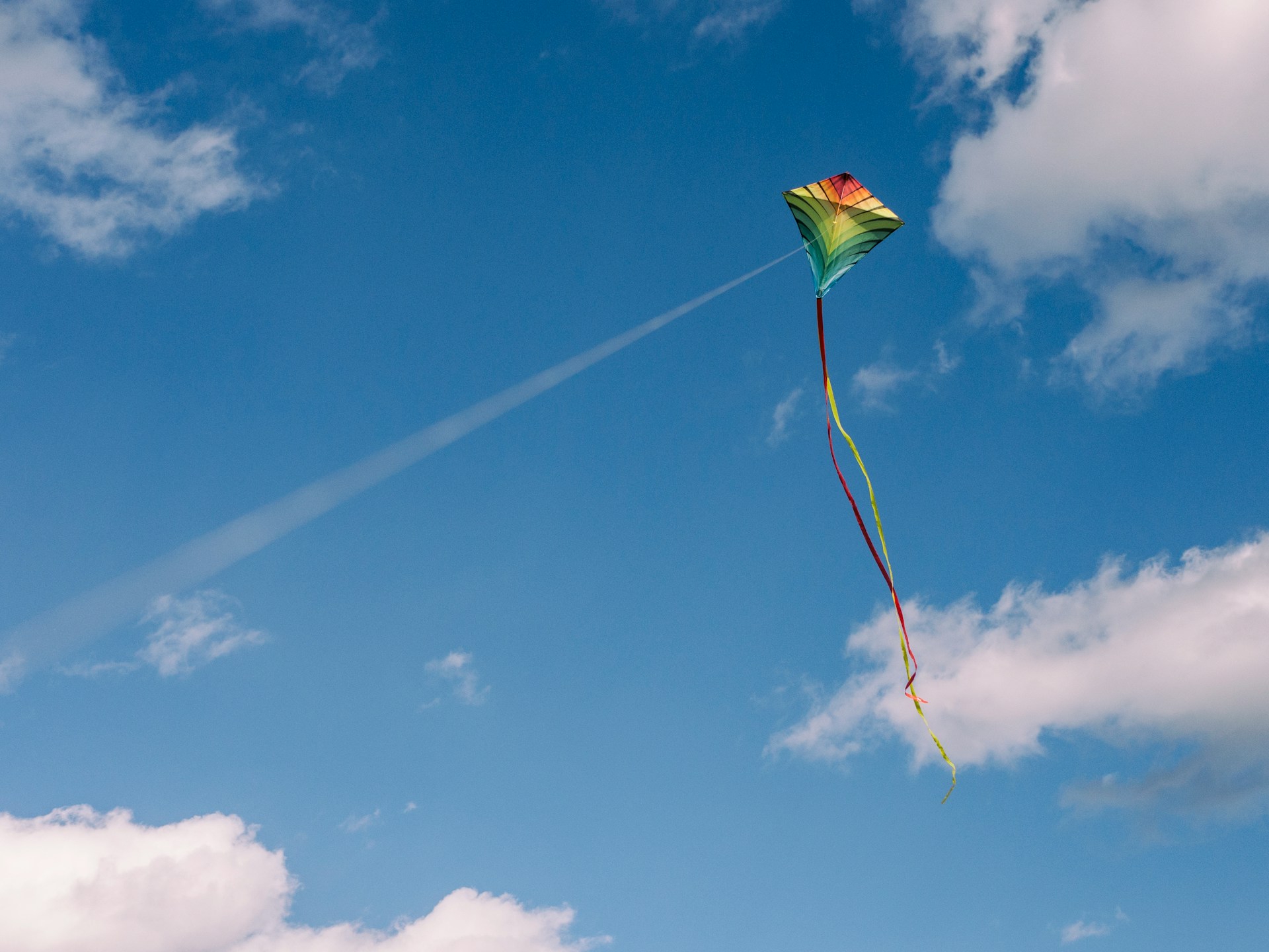 A colorful kite with red, yellow, and green shades soars in a clear blue sky with a few scattered white clouds, reminiscent of the calm found in mental health treatment. The kite has two long, trailing ribbons adding movement to the image.