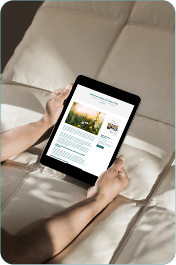 A person is holding a black tablet device while sitting on a beige cushioned surface. The tablet screen displays an article about mental health treatment featuring an image of flowers and text content. The person's hands and forearms are visible, but their face is not shown.