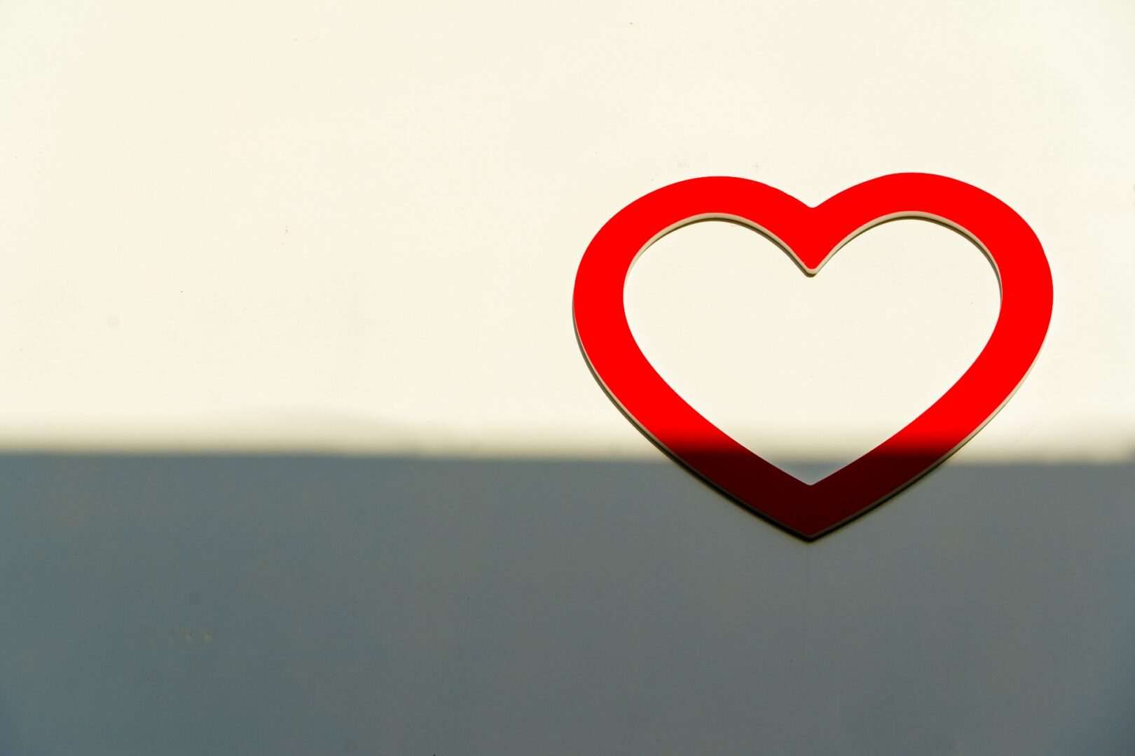 A red heart-shaped outline is positioned on a light-colored wall. Shadows cover the lower portion, creating a contrast with the bright heart, embodying the subtle conversation between healing and what’s wrong—a reflection of trauma-informed care.