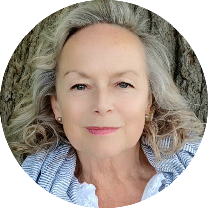 Portrait of an older woman with long, wavy gray hair, smiling softly. She is wearing a striped scarf over a white top, standing against a tree background, embodying the serene and nurturing essence often associated with Khiron Clinics' compassionate care.