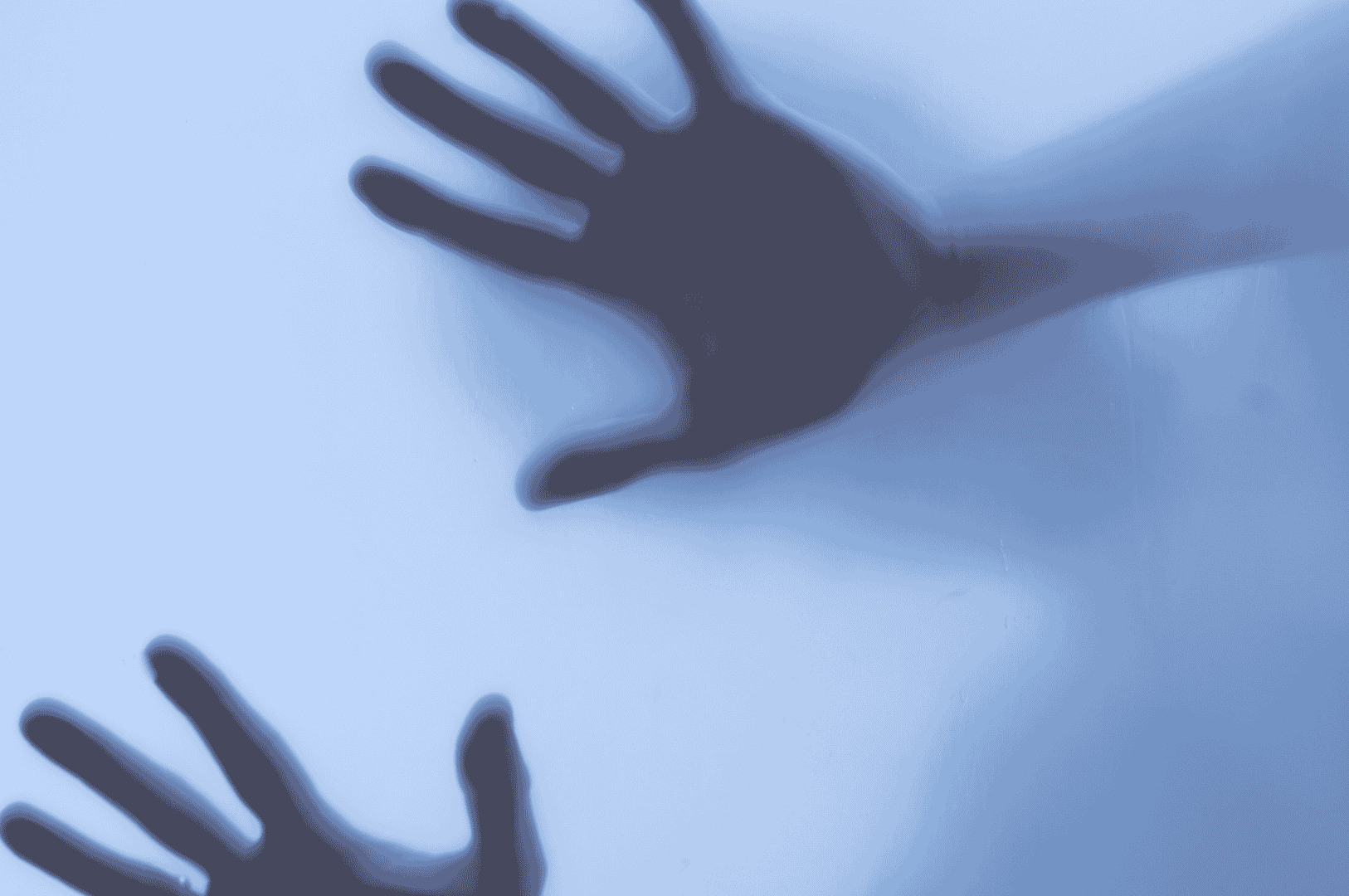 Silhouettes of two hands pressing against a translucent, blue-tinted surface capture a mysterious and eerie atmosphere, echoing the contours and placements of fingers and palms. This haunting image subtly suggests being stuck in a freeze response, evoking a sense of trapped trauma.