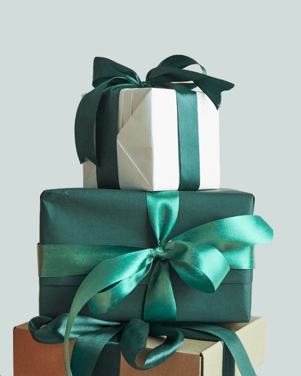 Three neatly wrapped gift boxes are stacked on top of each other, perfect for a festive brochure. The top two feature dark green ribbon bows, while the plain brown box at the bottom adds a charming contrast against the light grey background.