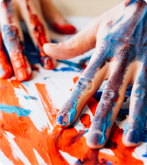 Close-up of two hands covered in blue and red paint, pressing and spreading color on a white surface—an abstract reflection that echoes the raw, expressive journey of asking, "What is Trauma?.