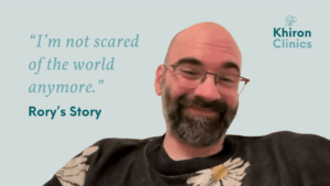 A smiling man with glasses and a beard sits in front of a light blue background. Text reads, “I’m not scared of the world anymore—no more hyperarousal or hypoarousal. Rory’s Story.” The Khiron Clinics logo is in the corner.