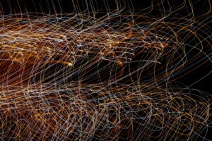 Colorful, swirling light trails of orange, white, and yellow overlap on a black background—an abstract, chaotic pattern with loops and curves throughout the image, visually echoing the complexities of understanding disorganized attachment.