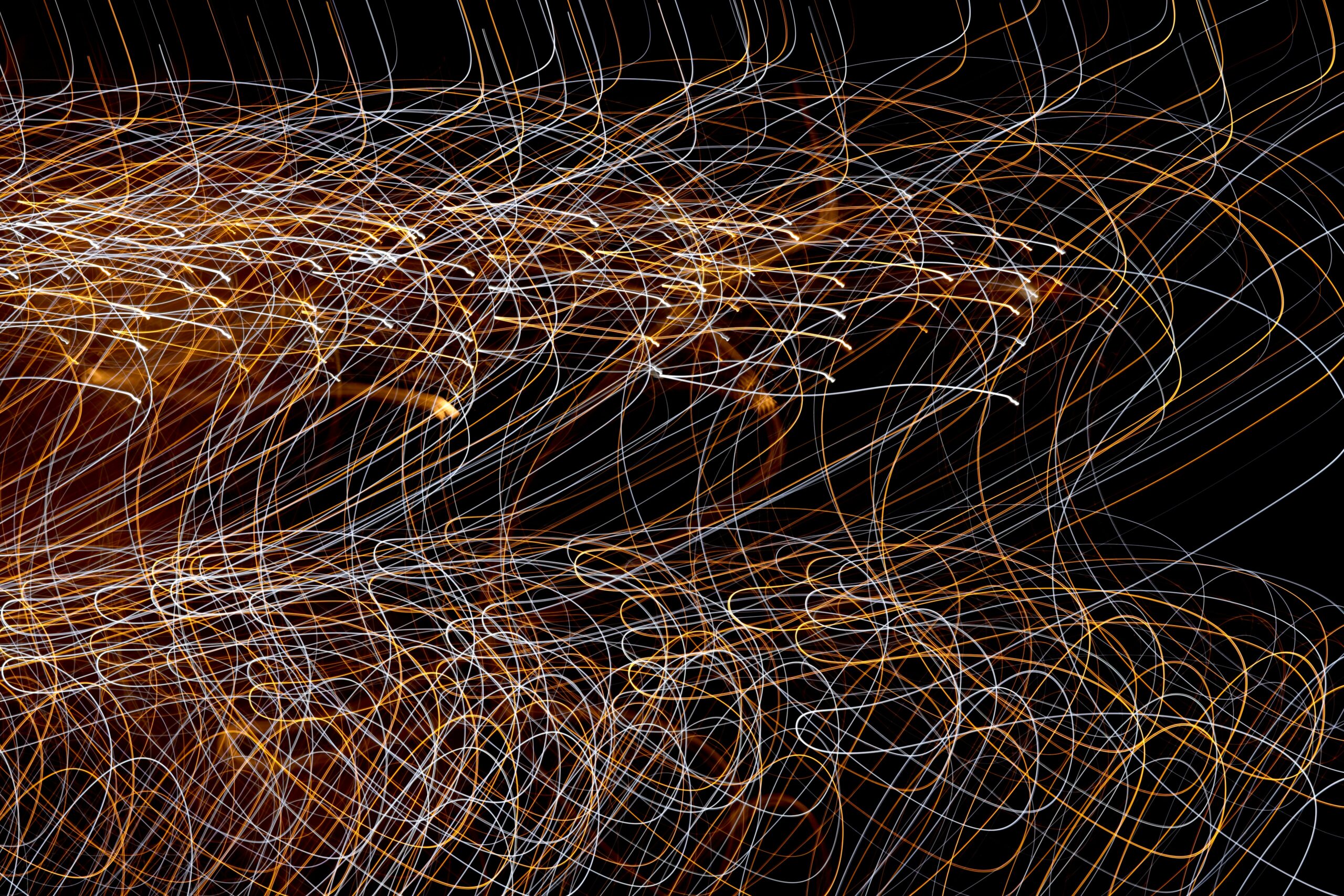 Colorful, swirling light trails of orange, white, and yellow overlap on a black background—an abstract, chaotic pattern with loops and curves throughout the image, visually echoing the complexities of understanding disorganized attachment.