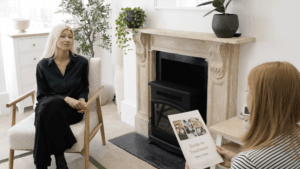 Trauma Therapist Anja Frykegaard speaking with a client in a calm therapy room at Khiron Clinics in London, with natural light, plants, and a fireplace, while the client holds a treatment guide booklet.