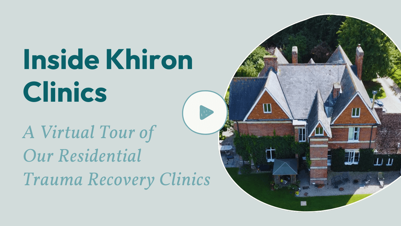 Aerial view of a large brick house with a grey roof, surrounded by greenery, next to text reading “Inside Khiron Clinics: A Virtual Tour of Our Residential Trauma Recovery Clinics – What is Trauma?” A play button icon is centred on the image.
