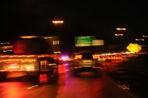 Blurry, night-time photo of cars and lorries on a wet motorway, with streaks of red and yellow lights—capturing the chaos and alertness that echo Understanding Trauma Responses: How Your Body Remembers Danger. Glowing street signs flicker in the background.