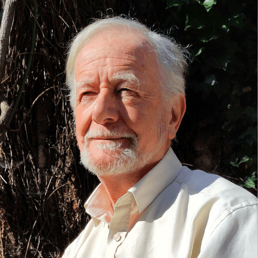 An older man with white hair and a beard, wearing a light-coloured shirt, stands outdoors in sunlight with greenery and a tree trunk behind him. He has a thoughtful expression, reflecting the compassionate care found at Khiron Clinics.