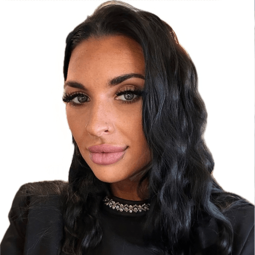 A woman with long, wavy dark hair, wearing a black top with a jewelled neckline, poses against a plain white background—an image often seen in profiles About Khiron Clinics. She has a nose piercing.