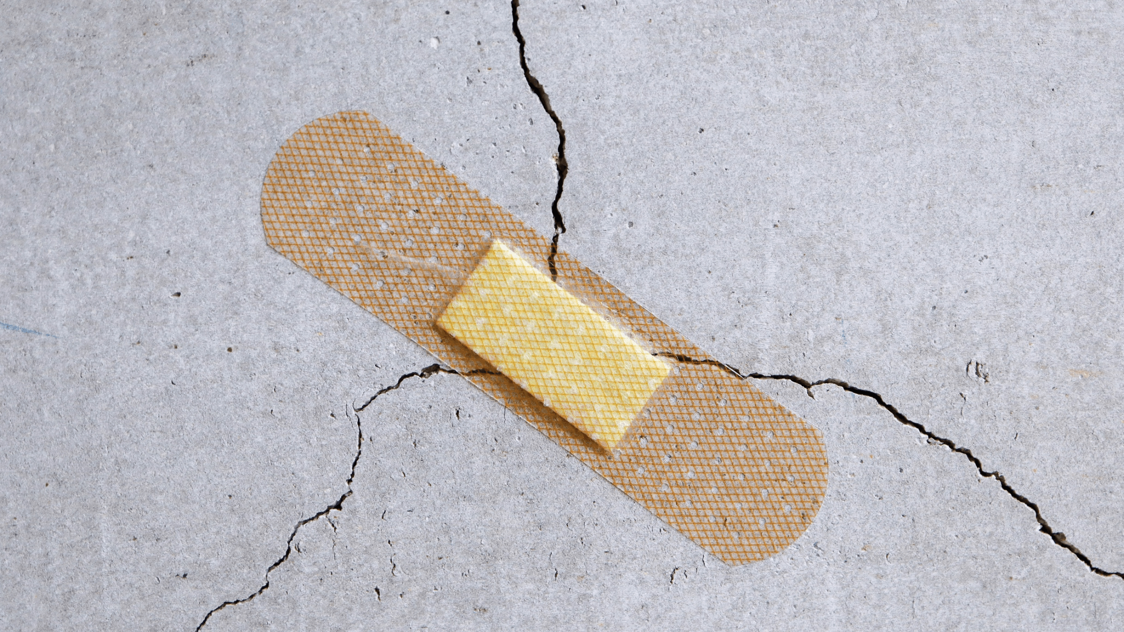 A beige plaster is placed over a crack in a grey concrete surface, as if attempting to repair the crack.