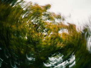 Swirling blur of green and yellow tree branches against a bright sky, evoking dizziness and a sense of spinning motion whilst suggesting the mind-body connection through abstract patterns. Depicting Anxiety and Dizziness: Understanding the Mind-Body Connection